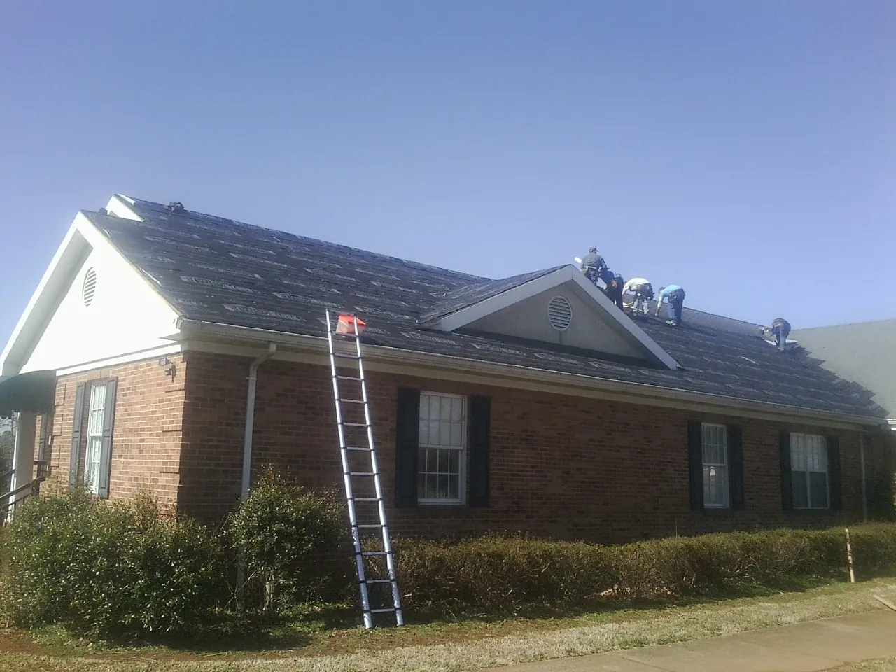 Crew tearing shingles off a brick ranch roof with a ladder set — Emergency Roof Repair work by our crew in Montclair